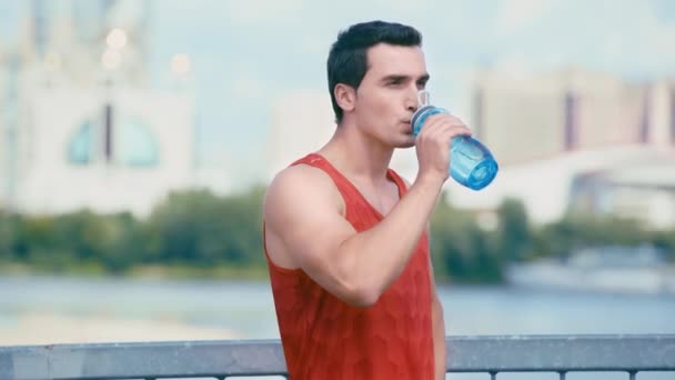 橋の上に立ってスポーツボトルから水を飲む若いスポーツマンは — ストック動画