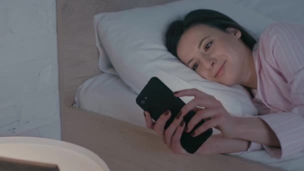 Chica Sonriente Usando Teléfono Inteligente Cerca Del Reloj Flor Mesita — Vídeos de Stock