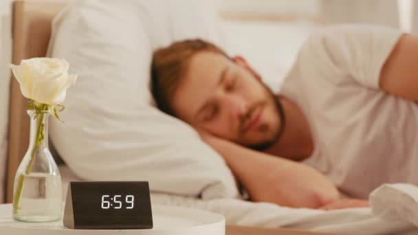 時計の選択的な焦点は ベッドサイドテーブルの上に上昇し 男は朝に寝て — ストック動画