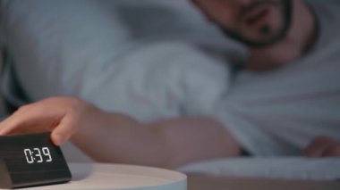 Geceleri yatakta uzanan bir adamın saate baktığı seçici odak.