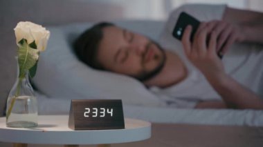Geceleri yatakta akıllı telefon kullanan gülümseyen adamın seçici odağı 