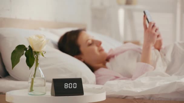 Relógio Rosa Mesa Perto Menina Sorridente Usando Smartphone Cama Manhã — Vídeo de Stock