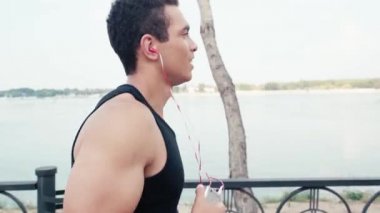 Kulaklıklı ve akıllı telefonlu sporcu sokakta koşuyor ve gülümsüyor.