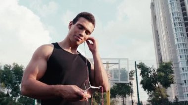 Sporcunun düşük açılı görüşü kulaklık takması ve sokakta gülümsemesi.