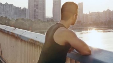 Sporcu başını çeviriyor, gülümsüyor ve köprüdeki kameraya bakıyor.