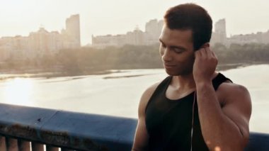 Sporcu gülümsüyor ve kulaklıklarını takıyor.