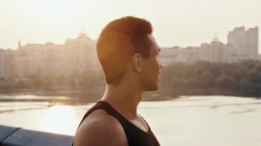 Sporcu köprüde koşuyor, gülümsüyor ve su içiyor.