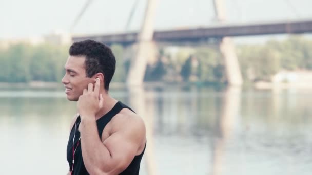 Спортсмен Слухає Музику Посміхається Дивиться Камеру Біля Річки Вулиці — стокове відео