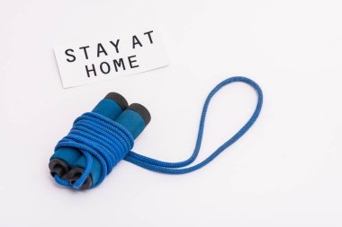 blue skipping rope near paper with stay at home lettering on white with copy space clipart