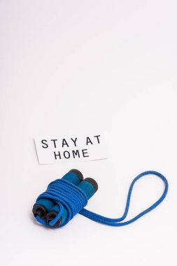 blue skipping rope near paper with stay at home lettering on white clipart