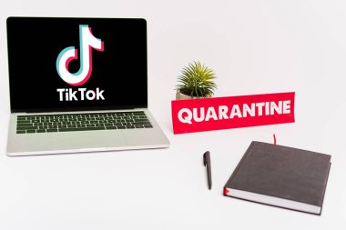 KYIV, UKRAINE - 8 Nisan 2020: Bitki, kalem, defter ve kağıdın yanında Tik tok web sitesi olan dizüstü bilgisayar beyaz üzerine karantina harfleri yazılı 