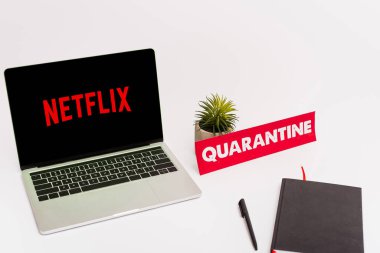 KYIV, UKRAINE - 8 Nisan 2020: Netflix web sitesi ile birlikte yeşil bitki, kalem, defter ve kağıt yakınında beyaz karantina harfleri ile ekranda 