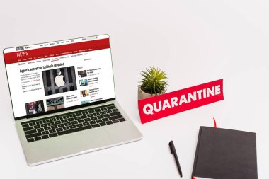 KYIV, UKRAINE - 8 Nisan 2020: beyaz üzerine karantina harfleri olan yeşil bitki, kalem, defter ve kağıdın yanında bbc haber sitesi olan laptop 