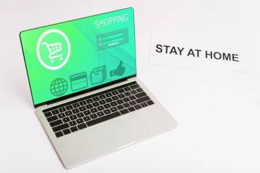 Bilgisayarı ve online alışveriş sitesi ekranda kağıdın yanında, evde kalıp beyaz harflerle yazılıyor. 