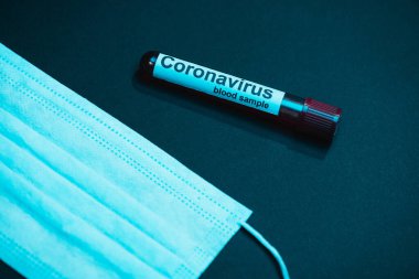 Koyu renk üzerinde Coronavirus kan örneği ve tıbbi maske olan test tüpünün yüksek açılı görüntüsü