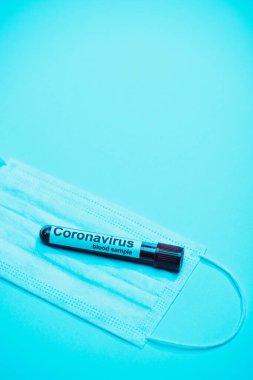 Mavi arka planda tıbbi maskenin üzerinde Coronavirus kan örneği bulunan test tüpünün yüksek açılı görüntüsü