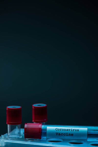 Пробирки с коронавирусной вакциной на стойке пробирки на тёмном фоне
