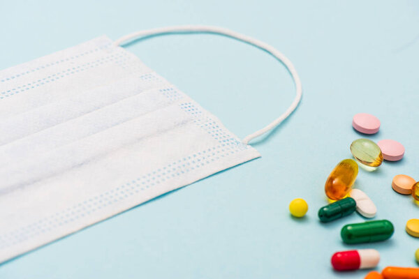 High angle view of medical mask near colorful pills on blue background