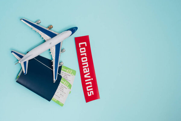 Top view of toy near card with coronavirus lettering and passports with air tickets on blue