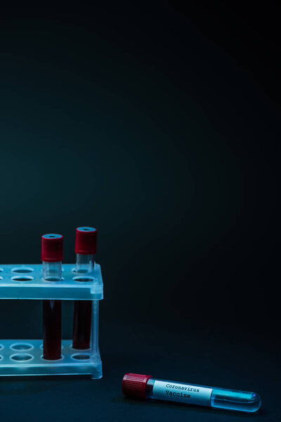 Коронавирусная вакцина возле стойки пробирки с образцами крови на тёмном фоне
