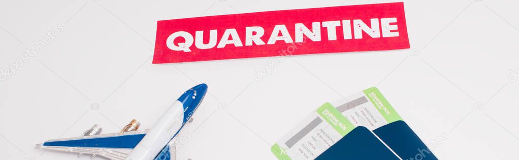 Panoramic shot of toy near card with quarantine lettering and passports with air tickets on white