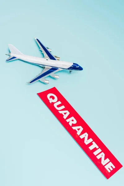 Avión de juguete pequeño cerca de papel con letras de cuarentena aisladas en azul - foto de stock
