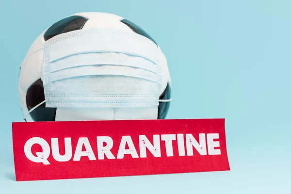 Calcio in maschera protettiva medica vicino carta rossa con scritta di quarantena su blu — Foto stock