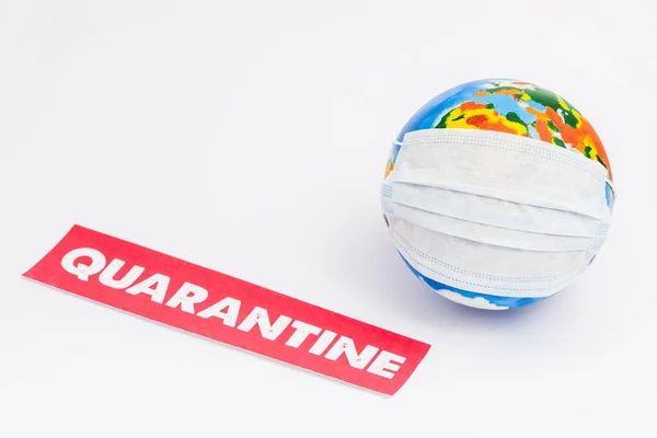 Globe in medical mask near red paper with quarantine lettering on white with copy space — Stock Photo