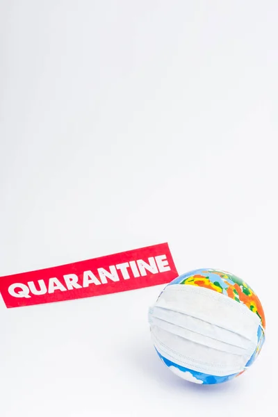 Globo em máscara médica perto de papel com letras de quarentena em branco — Fotografia de Stock