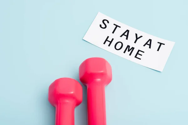 Pink dumbbells near paper with stay at home lettering on blue — Stock Photo