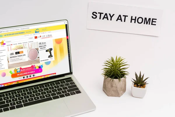 KYIV, UKRAINE - APRIL 8, 2020: laptop with aliexpress website on screen near plants and paper with stay at home lettering on white — Stock Photo