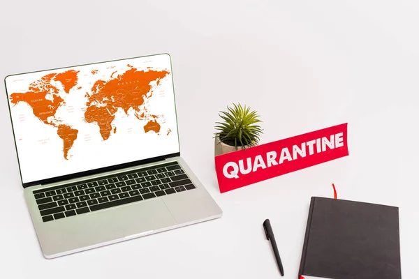 KYIV, UKRAINE - APRIL 8, 2020: laptop with world map on screen near plant, pen, notebook and paper with quarantine lettering on white — Stock Photo