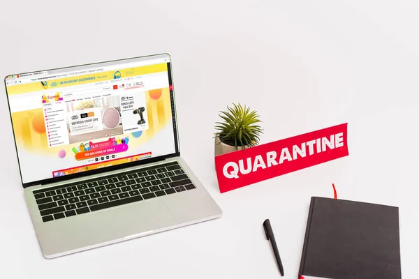 KIEW, UKRAINE - 8. April 2020: Laptop mit aliexpress-Website am Bildschirm in Werksnähe, Stift, Notizbuch und Papier mit Quarantäne-Schriftzug auf weiß — Stockfoto