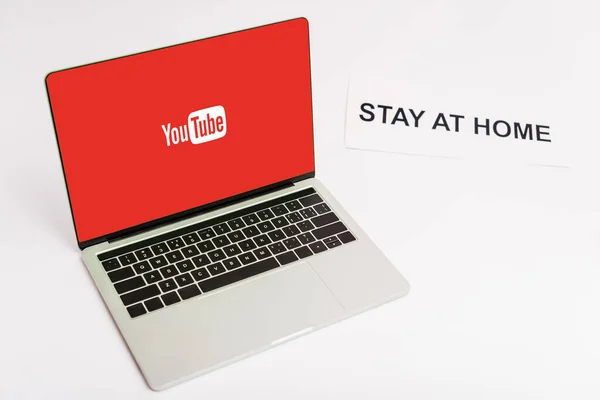 КИЕВ, УКРАИНА - 8 апреля 2020 года: ноутбук с вебсайтом YouTube на экране рядом с бумагой с домашней надписью на белом — стоковое фото