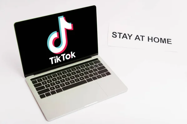 КИЕВ, УКРАИНА - 8 апреля 2020 года: ноутбук с tik tok веб-сайт на экране рядом с бумагой с пребывание дома буквы на белом — Stock Photo