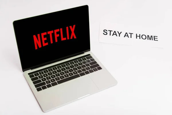 KYIV, UKRAINE - APRIL 8, 2020: laptop with netflix website on screen near paper with stay at home lettering on white — Stock Photo