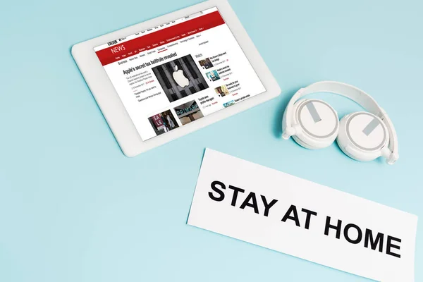 KYIV, UKRAINE - APRIL 8, 2020: digital tablet with bbc news app near headphones and paper with stay at home lettering on blue — Stock Photo