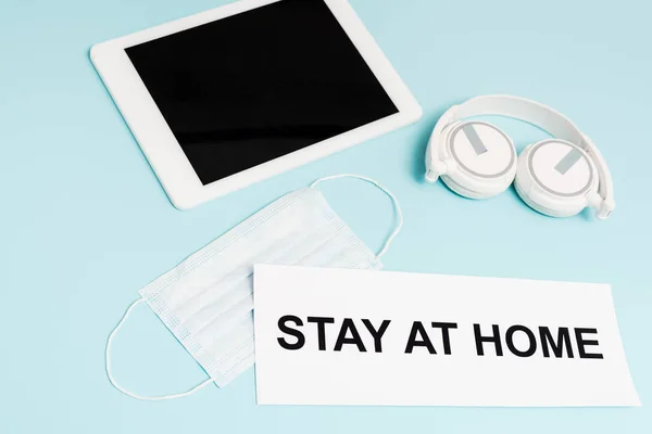 Tablet digital com tela em branco perto de fones de ouvido, máscara médica e papel com estadia em casa lettering em azul — Fotografia de Stock