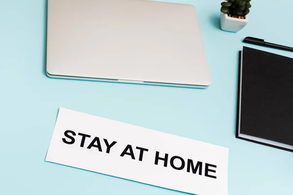 Laptop, notebook, caneta e planta perto de papel com estadia em casa lettering em azul — Fotografia de Stock