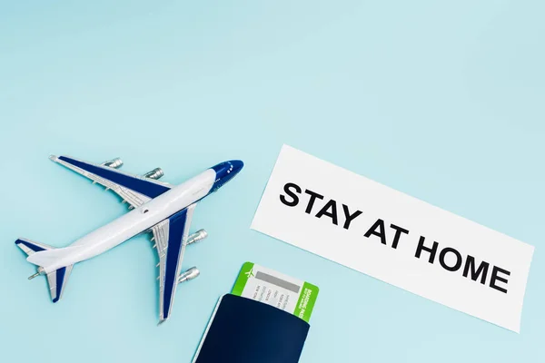 Vista superior del avión de juguete cerca de papel con letras de estancia en casa, pasaporte y tarjeta de embarque aislados en azul - foto de stock
