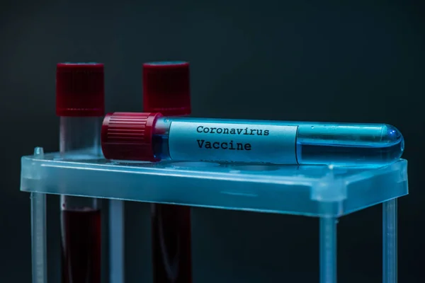 Coronavirus vaccine on test tube rack with sample tubes with blood on dark — Stock Photo