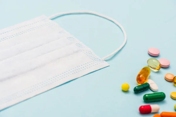 Vista de ángulo alto de la máscara médica cerca de píldoras de colores sobre fondo azul — Stock Photo