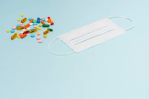 Vista de ángulo alto de la máscara médica cerca de píldoras brillantes sobre fondo azul — Stock Photo