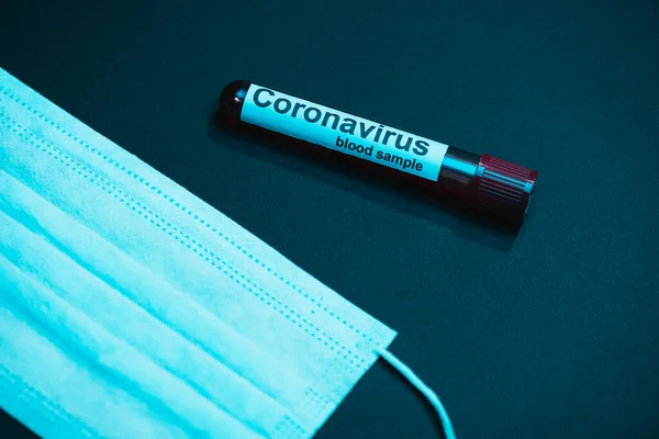 High angle view of test tube with coronavirus blood sample and medical mask on dark — Stock Photo