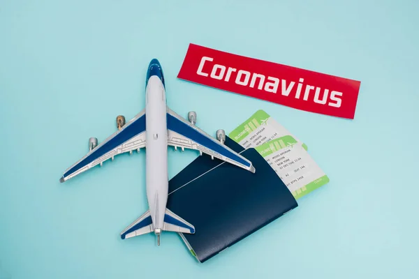 Vista superior del juguete cerca de la tarjeta con letras coronavirus y pasaportes con billetes de avión sobre fondo azul - foto de stock