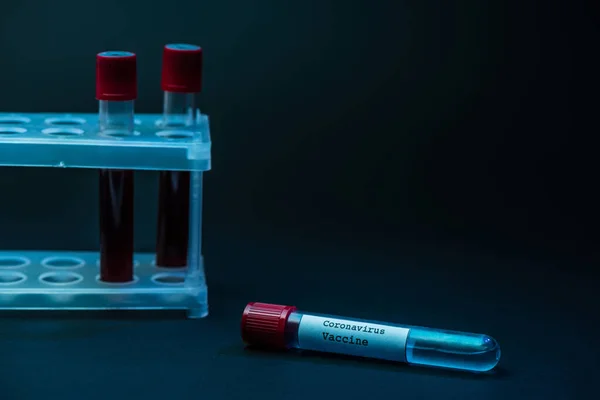 Coronavirus vaccine near test tube rack with blood samples on dark — Stock Photo