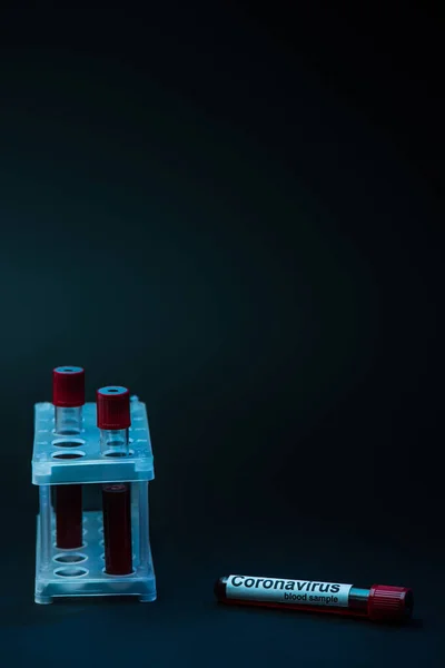 Coronavirus blood sample near test tube rack with tubes on dark background — Stock Photo