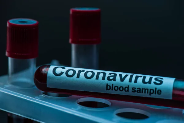 Mise au point sélective du tube à échantillon avec lettrage du sang du coronavirus sur le support du tube à essai sur fond sombre — Photo de stock