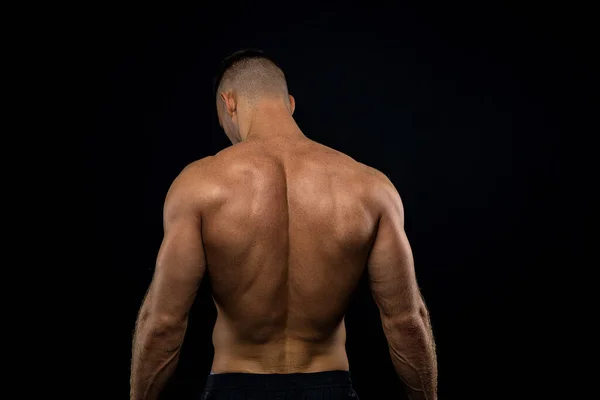 Мощный мускулистый спортсмен демонстрирует свою спину возле черной стены — стоковое фото