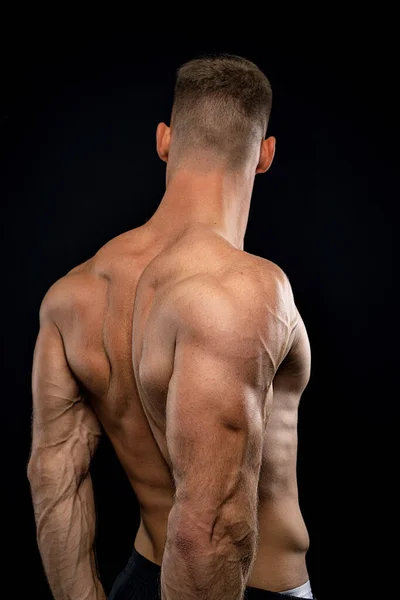 Puissant athlète musclé montre son dos à côté du mur noir — Photo